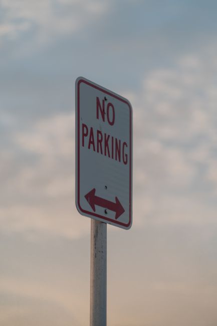 A blue parking sign indicating designated parking for people with disabilities, featuring a white wheelchair symbol and the word 'PARKING' in all caps. The sign includes additional details about legal
